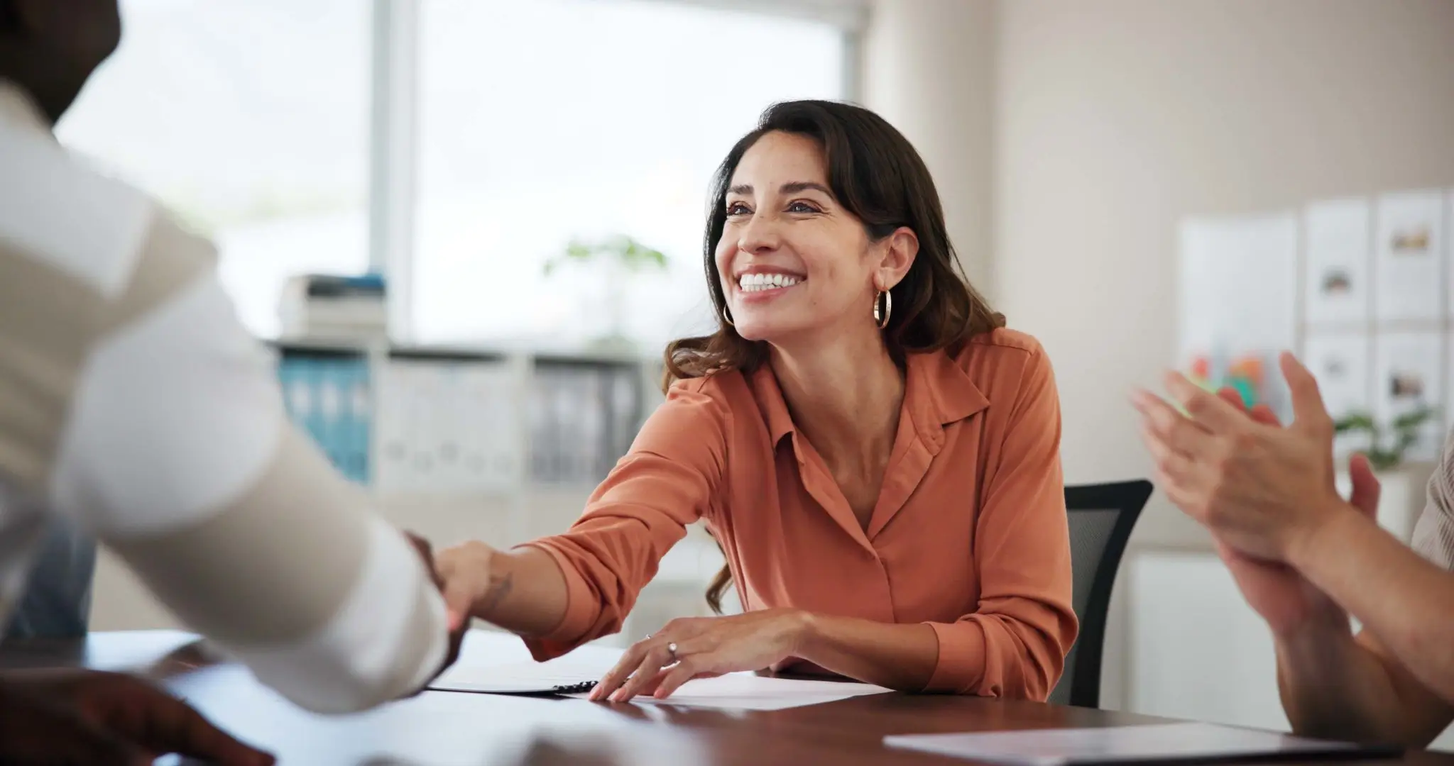 Woman smiling, shaking hands in office meeting.