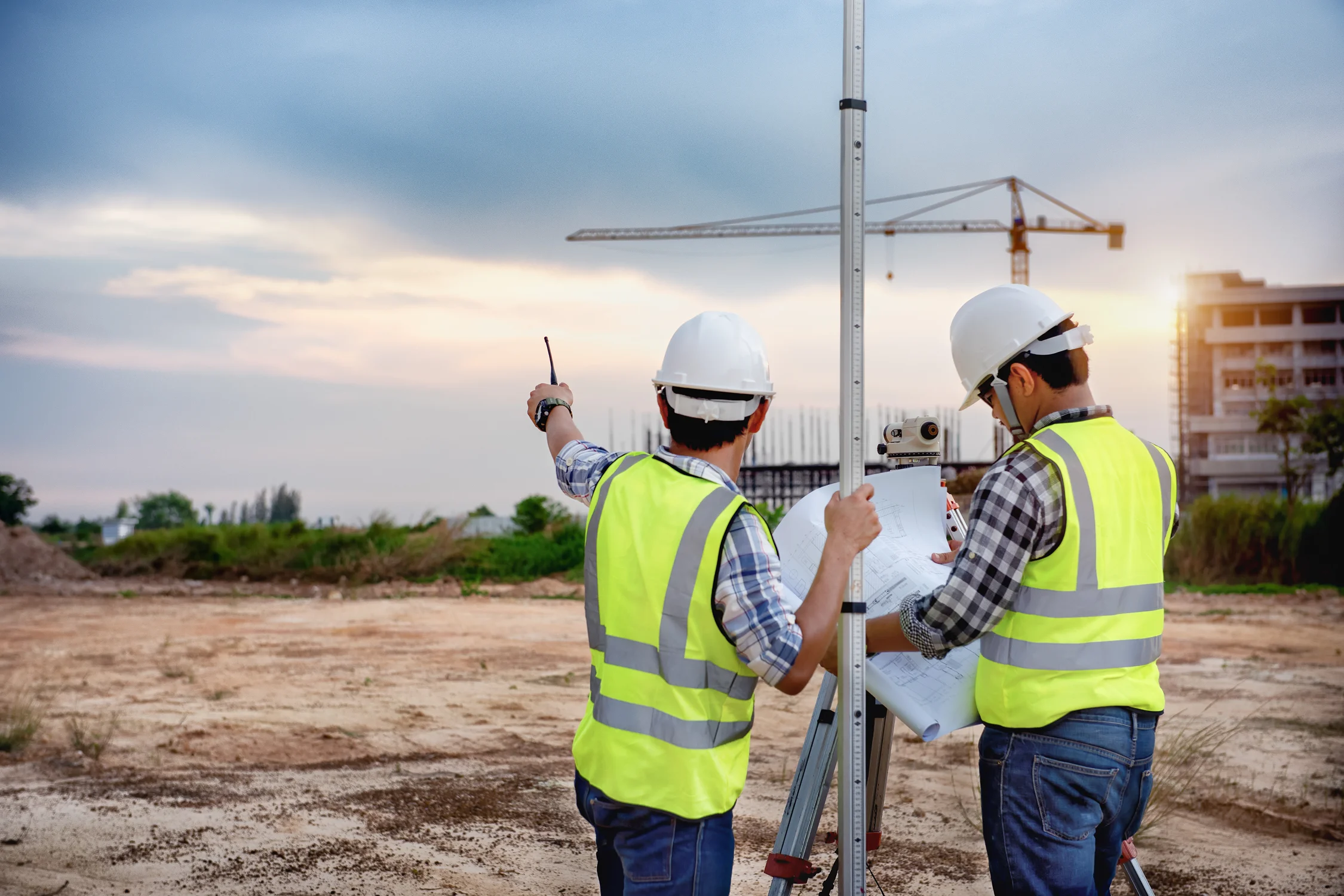 Surveyors working at construction site, sunset background.